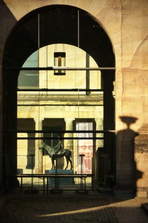Vue du Neues Museum à Berlin à travers une arche, avec reflet d’une statue équestre et affiche de Néfertiti